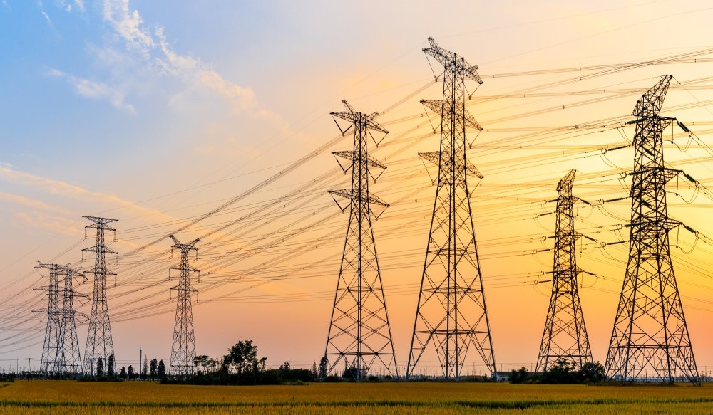 Multiple electricity pylons shown against a sunset backdrop.